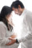 A beautiful maternity photo of a couple embracing and kissing, with their eyes closed and foreheads touching. They are standing in front of a plain white background, creating a simple and elegant aesthetic.