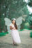 Young girl dressed in a white angel costume with a halo, wings, and a wand. She is smiling and looking off to the side
